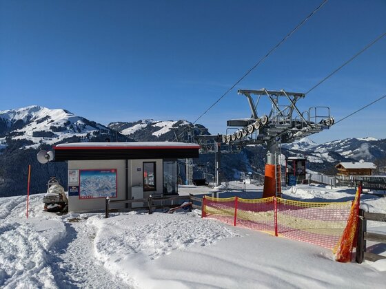 Bergstation eines Sessellifts im Winter mit verschneiten Gipfeln im Hintergrund.