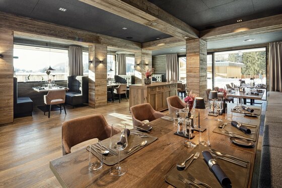 Alpenhotel Restaurant Innenansicht Moderner Restaurantraum mit Holzwänden, eingedeckten Tischen und großen Fensterfronten.