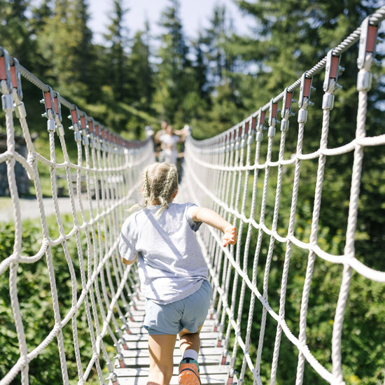 A girl is walking across a suspension bridge