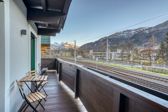 Balkonaussicht Apartment Tristkogel Holzbalkon mit Sitzgruppe und Blick auf Bahngleise sowie schneebedeckte Berge.