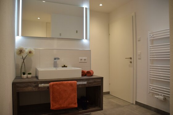 Badezimmer Apartment Sabrina Modernes Badezimmer mit weißem Aufsatzwaschbecken, großem Leuchtspiegel und Handtuchheizkörper.