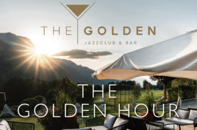 Ein eleganter Außenbereich mit Blick auf die Berge und einer sanften Sonnenuntergangsstimmung. Der Schriftzug "THE GOLDEN HOUR" kennzeichnet die entspannte Atmosphäre des Jazzclubs und der Bar.