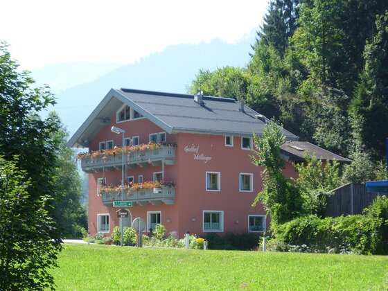 Mehrstöckiges, rosa Gebäude mit Blumenbalkonen vor bewaldetem Hang.