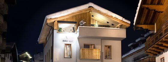 Doris' Nest bei Nacht Beleuchtetes alpines Gebäude bei Nacht mit schneebedecktem Dach und Holzfassade im Giebelbereich.