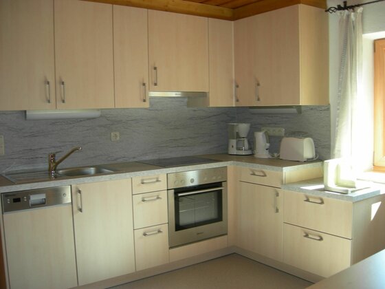 Küche im Haus Bergschmied Moderne Einbauküche in L-Form mit hellen Holzfronten, Herd, Backofen und Kaffeemaschine.