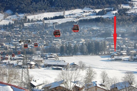 Blick auf eine Seilbahn mit roten Gondeln über einem verschneiten Dorf im Tal.