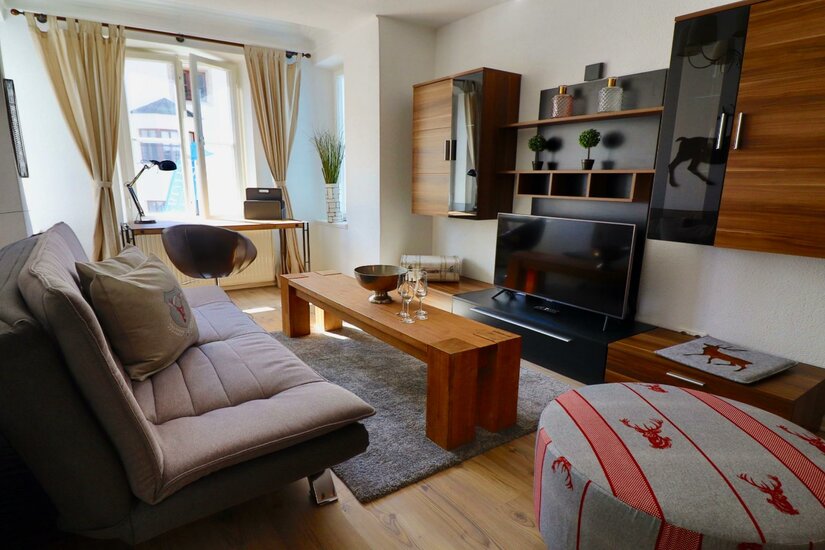 Wohnbereich Belle Kitz Pure Modernes Wohnzimmer mit Sofa, Holztisch, Fernseher und Schreibtisch am Fenster.