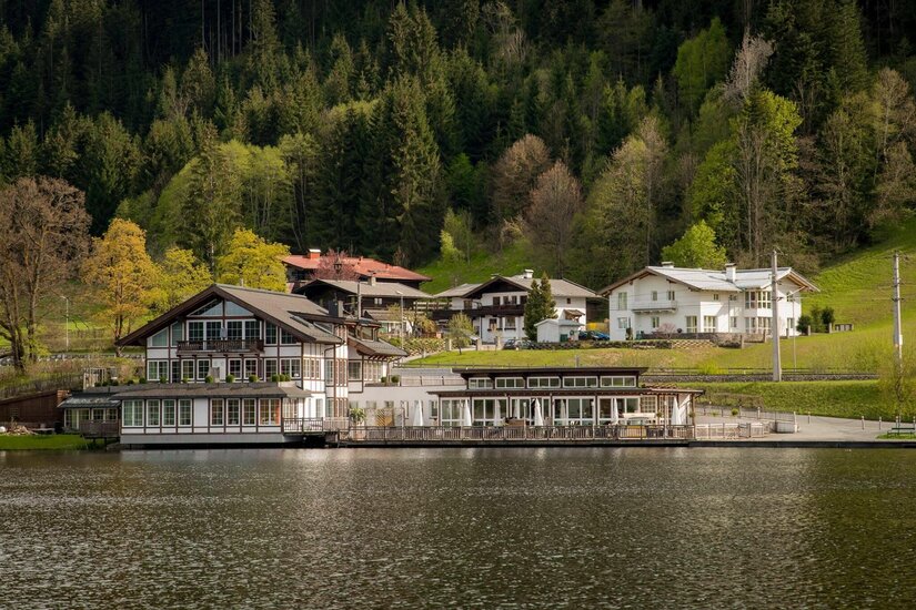 Pipino's Restaurant am See Restaurantgebäude mit Terrasse direkt am Seeufer vor bewaldetem Hang.
