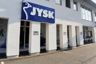 Außenansicht einer JYSK-Filiale mit blauem Logo an einer weißen Fassade.