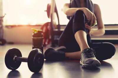 Physiotherapie und Krafttraining Eine Person sitzt am Boden eines Fitnessraums neben einer Hantel und einer Trinkflasche.