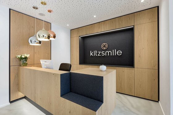 Moderner Empfangstresen aus Holz mit Logo-Schriftzug an der Rückwand und drei Hängeleuchten.