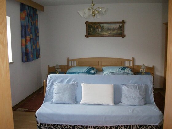Schlafzimmer im Haus Schuh Schlafzimmer mit Doppelbett aus Holz und davorstehendem hellblauem Sofa mit Kissen.