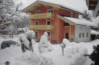 Ein mehrstöckiges, orangefarbenes Gästehaus mit Holzbalkonen in einer tief verschneiten Winterlandschaft.