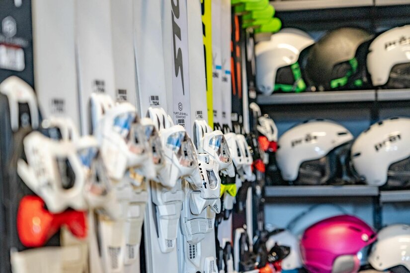 Skiverleih Kitzsport Nahaufnahme von aufgereihten Skiern mit Bindungen und Skihelmen in einem Regal.