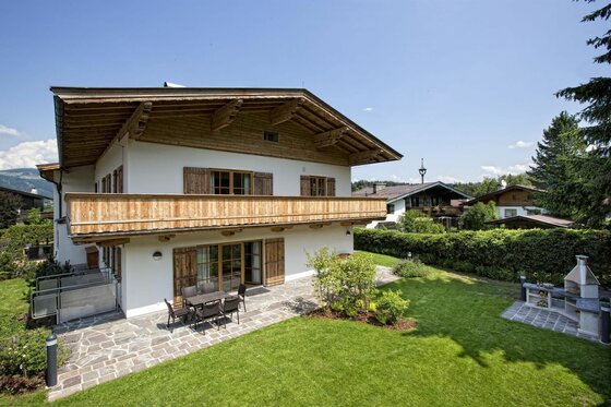 Zweistöckiges Landhaus mit Holzbalkon, Steinterrasse und Garten mit Außenkamin.