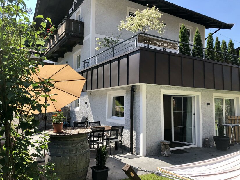MyApart Jochberg Außenansicht Außenansicht eines Ferienhauses mit Terrasse, Sonnenschirm, Sitzgruppe und großem Balkon.