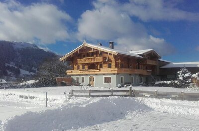 Fichterhof Kitzbühel im Winter Ein traditionelles Holzhaus mit Balkonen in einer verschneiten Winterlandschaft vor Bergen.