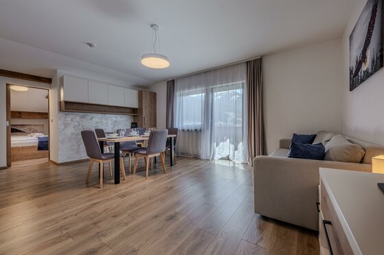 Moderner Wohn- und Essbereich mit Holzboden, Esstisch, Sofa und Blick auf einen Balkon.