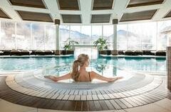 <p>Der Spa Bereich vom Grand Tirolia Kitzbühel mit einem großen Pool und Blick auf die Kitzbüheler Berge. Eine Frau sitzt am Rand des Pools und genießt die ruhige Atmosphäre.</p>