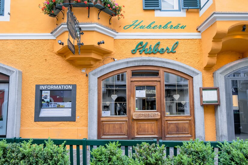 Huberbräu Ein einladendes Restaurant mit einer hellgelben Fassade und grünen Akzenten. Die Fenster sind mit Blumenkästen geschmückt.