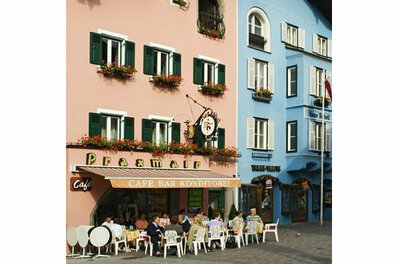 Außenansicht eines Cafés mit Gästen an Tischen vor einer rosa und blauen Hausfassade.