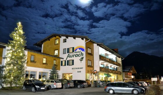 Beleuchtetes Hotel Aurach bei Nacht mit Parkplatz und geschmücktem Weihnachtsbaum.