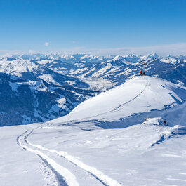 In the Südberge mountains within the Kitzbühel ski area, a ski tourer stands on a snow-covered peak and looks out over the surrounding mountains.