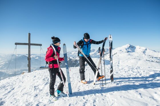 Skitour an der Bichlalm Zwei Skitourengeher am Gipfelkreuz im Schnee beim Abfellen der Skier.
