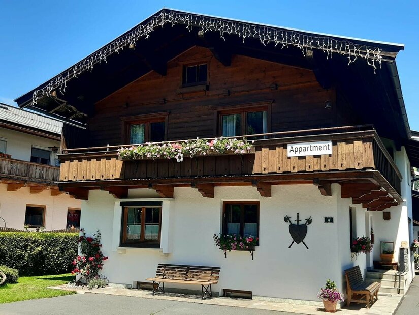 Reason Außenansicht Zweistöckiges alpines Haus mit dunkler Holzfassade im Obergeschoss und weißem Erdgeschoss.