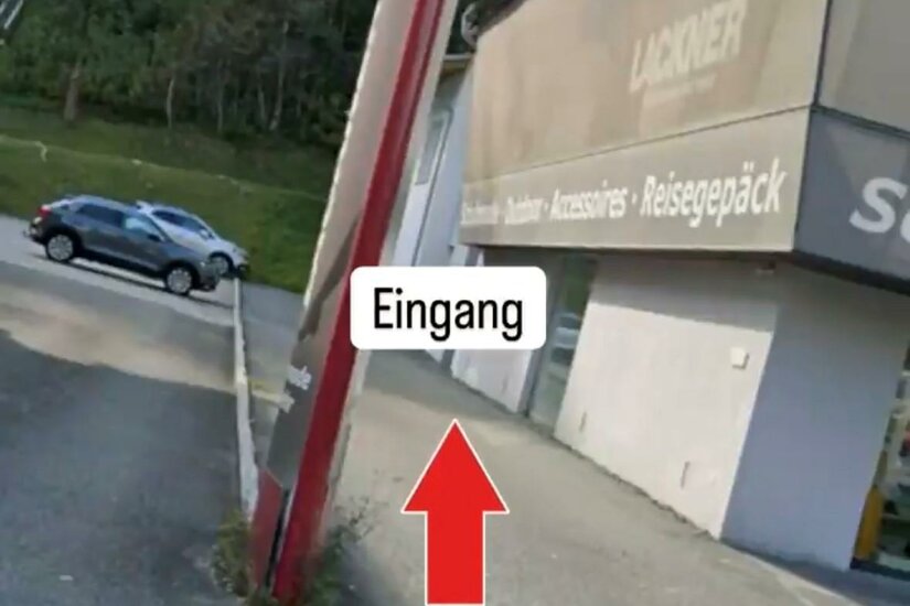Außenansicht eines Geschäftsgebäudes mit Parkplatz und Hinweisschild zum Eingang.