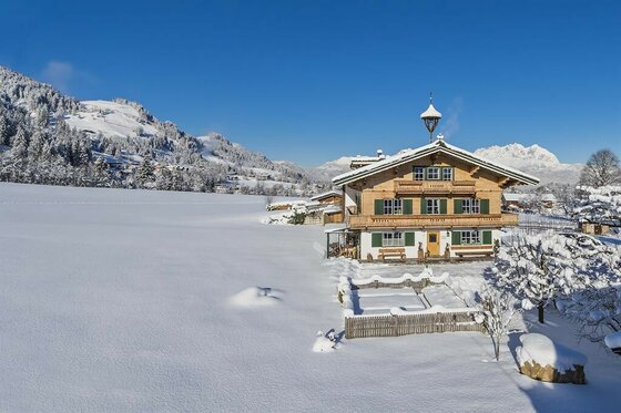 Lindenhof Kitzbühel im Winter Traditionelles Holzhaus in einer verschneiten Alpenlandschaft unter blauem Himmel.