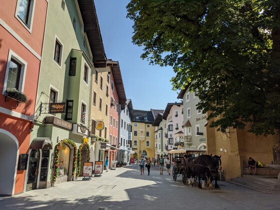 Altstadtgasse in Kitzbühel Blick in eine gepflasterte Altstadtgasse mit bunten Häuserfassaden und einer Pferdekutsche im Vordergrund.