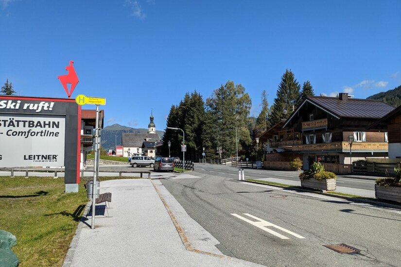 Bushaltestelle an einer Straße mit Schildern der Wagstättbahn und Blick auf eine Kirche im Hintergrund.
