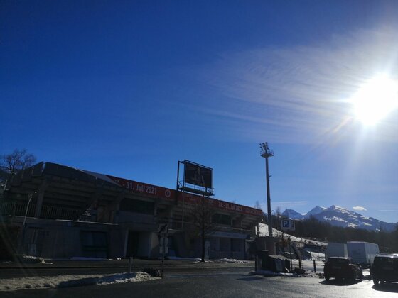 Stadion Buchenwald im Winter Außenansicht eines Stadions mit Flutlichtmast vor schneebedeckten Bergen unter blauem Himmel.