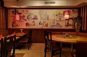 Innenansicht eines China-Restaurants mit runden Holztischen und einer großen Wandmalerei mit asiatischen Motiven.