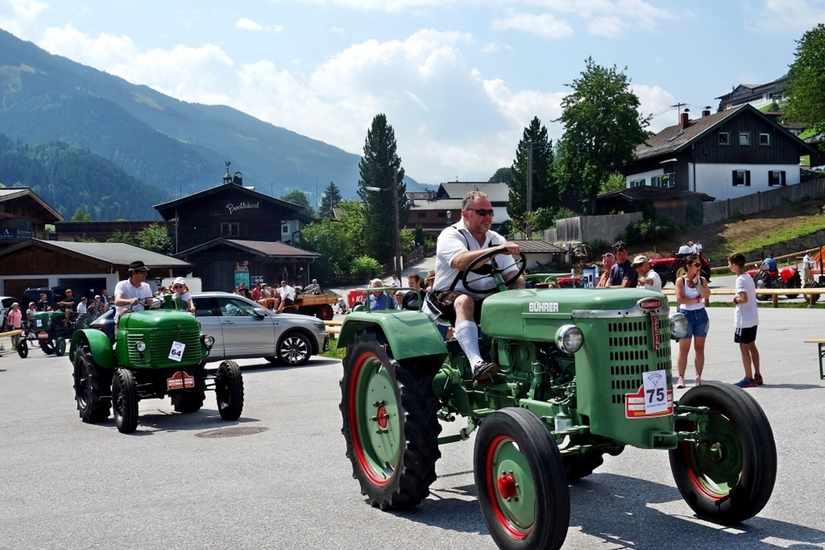 Oldtimertreffen Jochberg Eine große Versammlung von Traktoren in verschiedenen Farben, darunter Rot und Grün. Im Hintergrund sind auch klassische Autos und viele Menschen zu sehen.