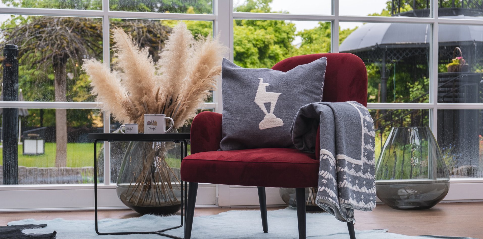 An armchair with a grey cushion with a chamois print and a beautiful green garden in the background