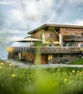 Modernes Berghaus aus Holz mit großer Terrasse vor Gebirgspanorama.