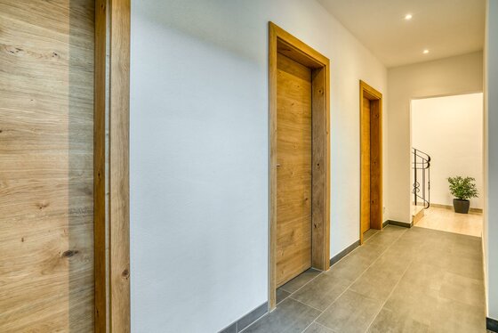 Eingangsbereich mit Abstellräumen Moderner Flur mit hellen Holztüren, grauen Bodenfliesen und weißer Wand.