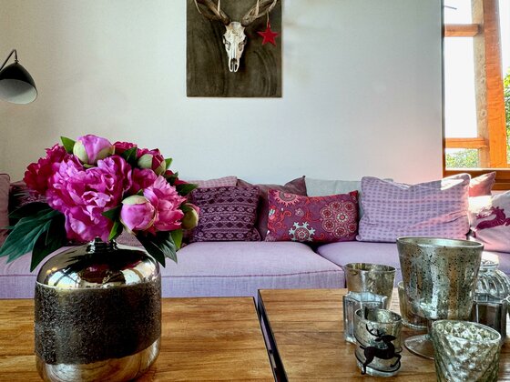 Ein modernes Wohnzimmer mit einem gemütlichen Sofa und bunten Kissen. Auf dem Tisch stehen eine Blumenvase und verschiedene dekorative Kerzenhalter.