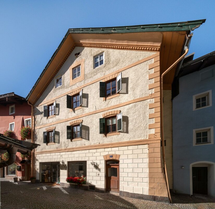 Ein charmantes, mehrstöckiges Gebäude mit bunten Fenstern und einem traditionellen Dach. Die Fassade ist in warmen Farben gehalten und es gibt Pflanzen vor dem Eingang.