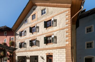 Ein charmantes, mehrstöckiges Gebäude mit bunten Fenstern und einem traditionellen Dach. Die Fassade ist in warmen Farben gehalten und es gibt Pflanzen vor dem Eingang.