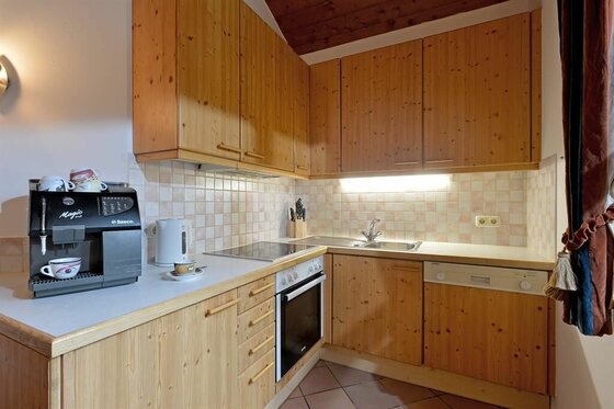 Küche im Appartement Holzleitner Kleine Einbauküche aus hellem Holz mit Kaffeemaschine, Herd und Spülbecken.