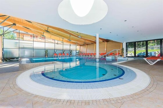 Hallenbad mit rundem Whirlpool im Vordergrund und Liegestühlen am Beckenrand.