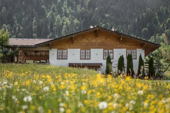 Landgasthof Reitherwirt Zur Andrea Ein weißes Gebäude mit Holzgiebel hinter einer blühenden Blumenwiese vor bewaldetem Hintergrund.