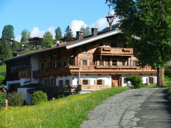 Traditioneller Bauernhof aus Holz und Stein mit Balkonen vor einer grünen Wiese.