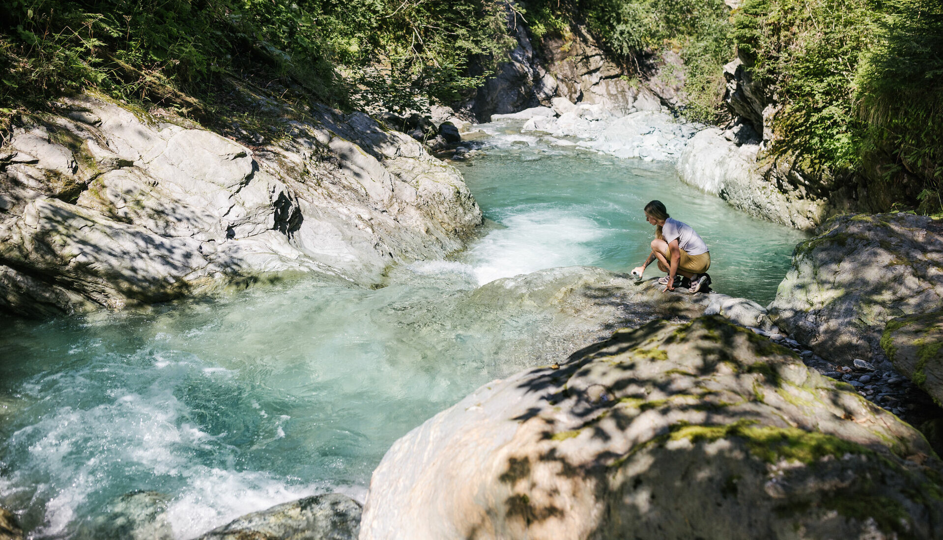 Person, die auf einem Felsen sitzt und aufs Wasser schaut