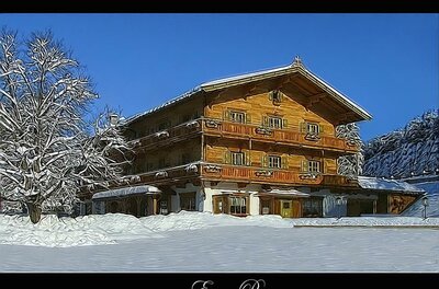 Ein mehrstöckiges Holzgebäude im alpinen Stil in einer verschneiten Winterlandschaft unter blauem Himmel.