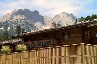 Holzhaus vor Bergpanorama Rustikales Holzhaus mit Schindeldach vor einer markanten Felskulisse der Alpen.