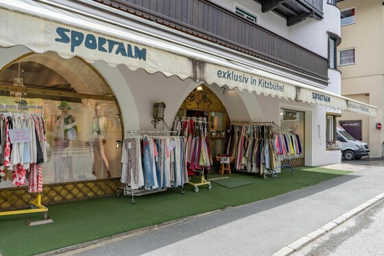 Sportalm Kitzbühel Ladengeschäft Außenansicht eines Bekleidungsgeschäfts mit Markise und Kleiderständern vor dem Eingang.